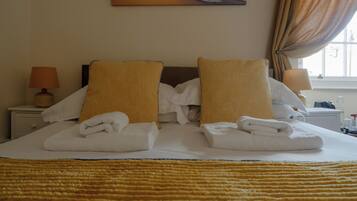 A hotel room with a bed, pillows, a nightstand, a lamp, and a window with curtains.