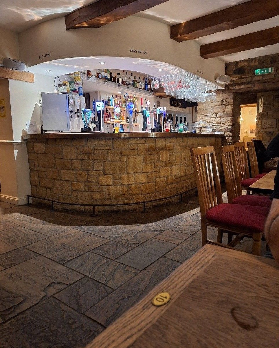A bar area with a stone counter, wooden chairs, and a sign indicating a service area.