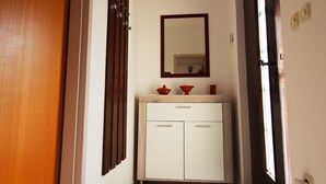 A narrow hallway with a wooden door on the left, a white cabinet with drawers and a mirror above it, and a window on the right. - Apartment for two person near the sea and city center,WIFI,airconditioning,BBQ,parking (Pula)