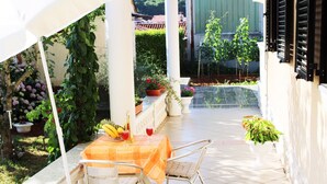An outdoor patio with a table set for two, surrounded by potted plants and a view of a garden. - Apartment for two person near the sea and city center,WIFI,airconditioning,BBQ,parking (Pula)