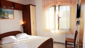 A neatly made bed with pillows and towels, a wooden chair, a painting on the wall, and a window with curtains. - Apartment for two person near the sea and city center,WIFI,airconditioning,BBQ,parking (Pula)