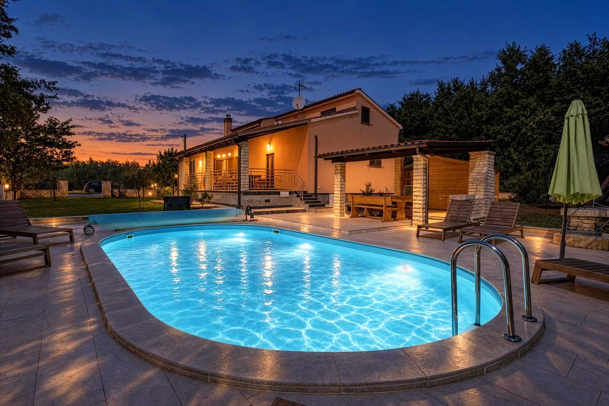 Piscina com deck de pedra, cadeiras de descanso e área de estar com um edifício ao fundo.