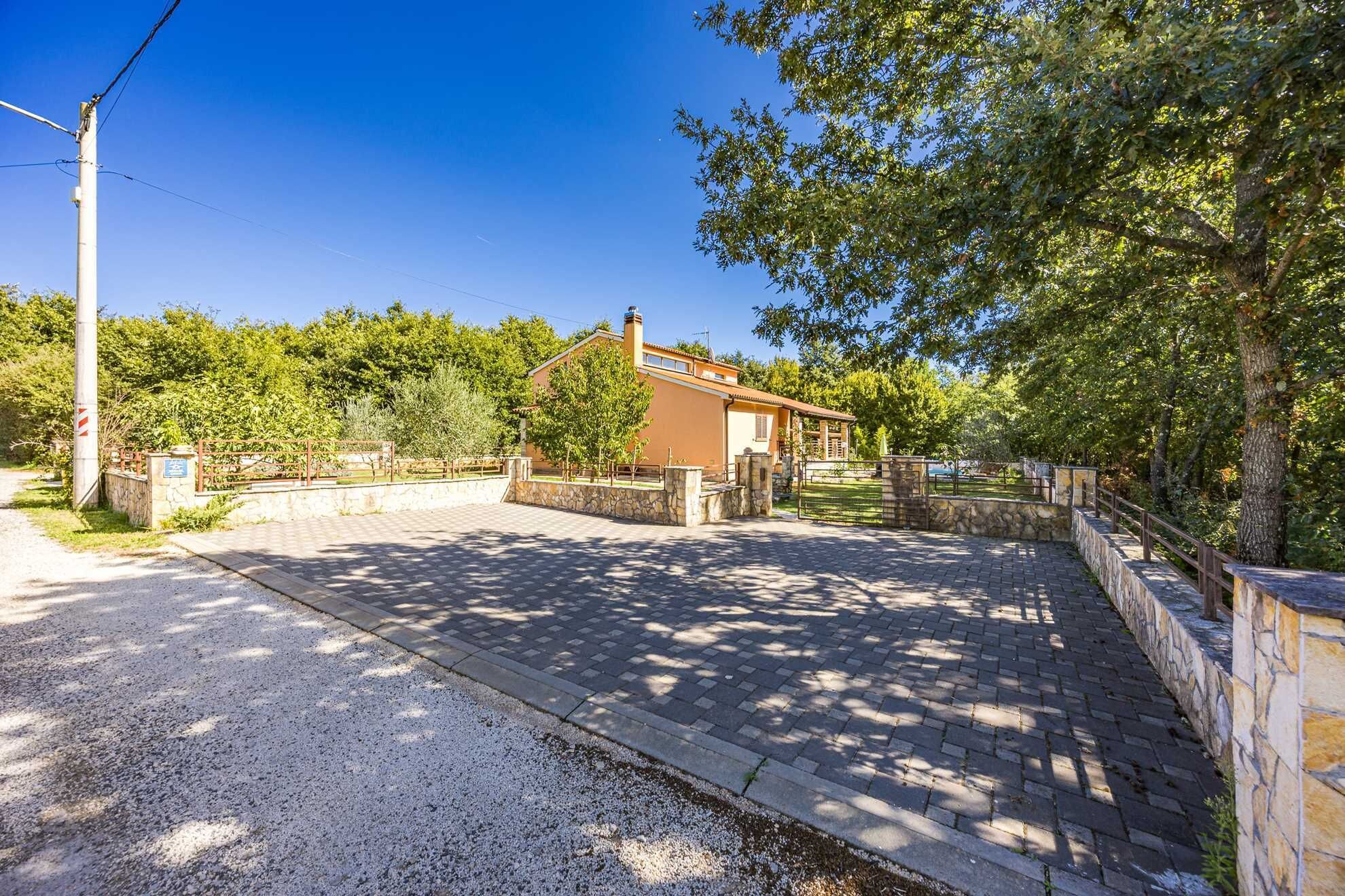 A residential property with a paved driveway, stone walls, and a house with a tiled roof.