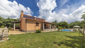 Une maison de plain-pied avec un toit en tuiles, une piscine et un mur en pierre.
