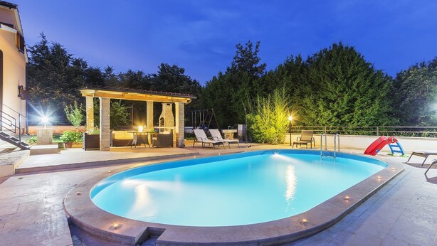 Une piscine agrémentée d’une pergola et de chaises longues, le tout entouré d’arbres.