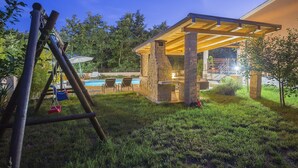 Un espace extérieur abrité comprenant une piscine, des piliers en pierre et une balançoire.