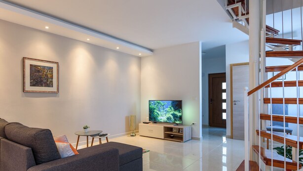 Een moderne woonkamer met een grijze bank, een flatscreen televisie en een trap.