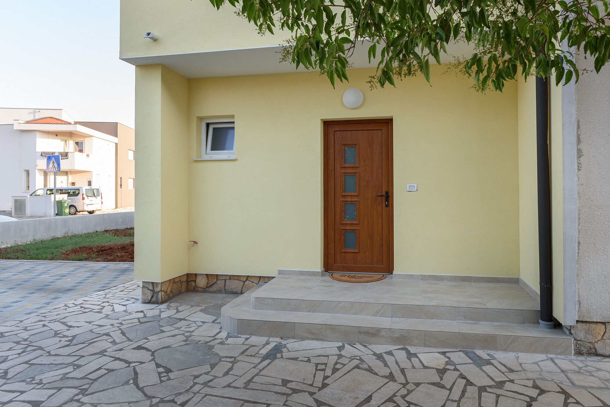 A yellow building with a wooden door, stone steps, and a small window.