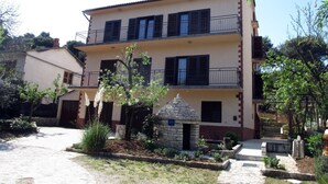 A multi-story building with balconies, a stone structure in front, and a paved courtyard.
