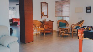 A modern living room with a sofa, two wicker chairs, a wooden cabinet, a mirror, and a foosball table. - Bright Villa 20mtrs from the sea (Comunidad Valenciana)