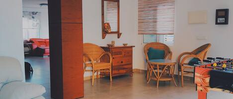 A modern living room with a sofa, two wicker chairs, a wooden cabinet, a mirror, and a foosball table.
