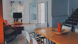 A modern living room with a wooden dining table, several chairs, a television, and a staircase. - Bright Villa 20mtrs from the sea (Comunidad Valenciana)