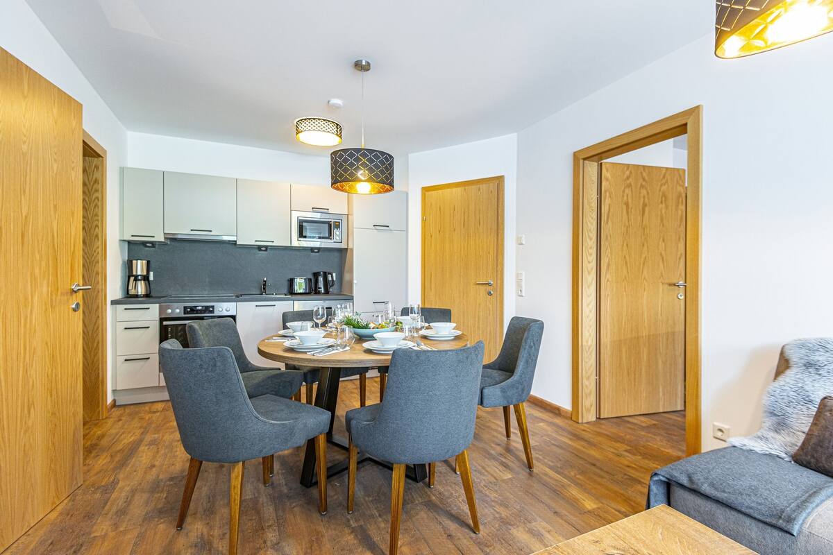 A modern kitchen with white cabinets, a dining table set for four, and a wooden door.