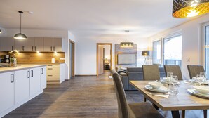 A modern kitchen with wooden flooring, white cabinets, and a dining area with a wooden table set for four. - Haus Bergblick (Bad Hofgastein)