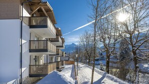 A snow-covered pathway leading to a multi-story building with balconies and a clear view of mountains in the background. - Haus Bergblick (Bad Hofgastein)