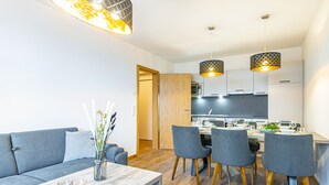 A modern living room with a grey sofa, a wooden coffee table, and a dining area with grey chairs and a wooden table. - Haus Bergblick (Bad Hofgastein)