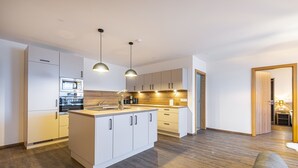 A modern kitchen with white cabinetry, a central island, and pendant lighting. - Haus Bergblick (Bad Hofgastein)