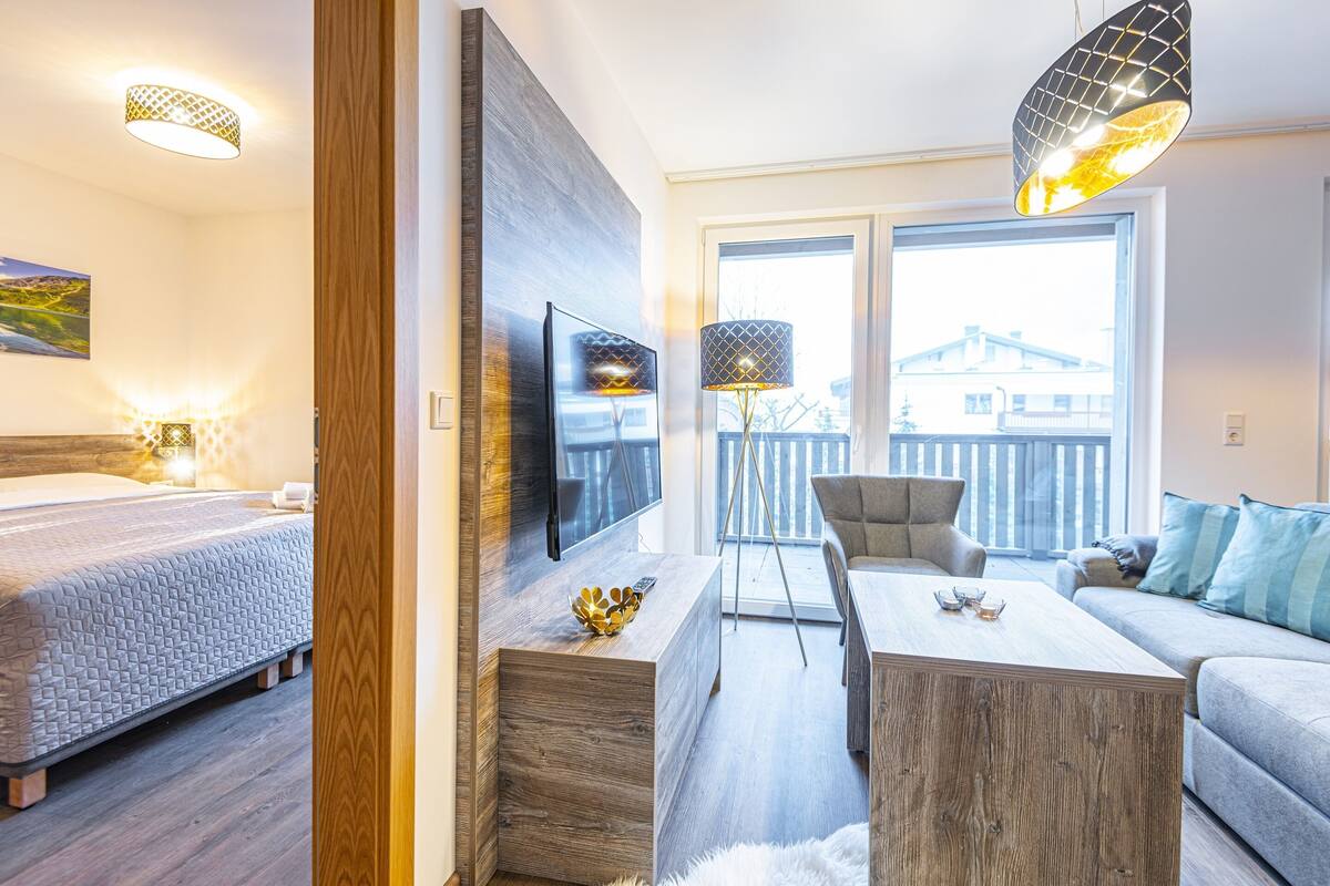 A modern hotel room with a bed, a TV, a wooden coffee table, a sofa, and a balcony with a view.