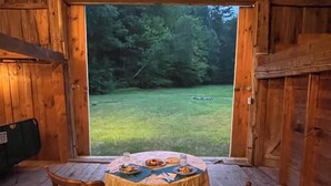 A wooden cabin with a dining table set for two, surrounded by wooden walls and a large window overlooking a grassy area. - Wonderful Views and Mountain Charm and on Beautiful 50 Acre Farm (Thornton)