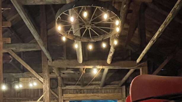 A rustic wooden cabin with a dining area, a large wheel chandelier, and a view of a lake. - Wonderful Views and Mountain Charm and on Beautiful 50 Acre Farm (Thornton)