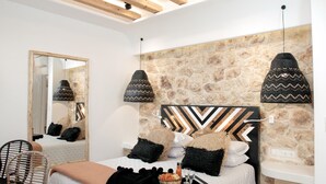 Een moderne slaapkamer met een schuine plafond, een accentmuur van steen, een bed met veel kussens, een nachtkastje en een grote spiegel.