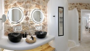 Een badkamer met een stenen muur, twee zwarte wastafels en twee ronde spiegels met verlichting.