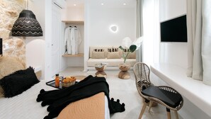 Een moderne hotelkamer met een bed, een zithoek met een bank en stoelen, een televisie en een groot raam met gordijnen.