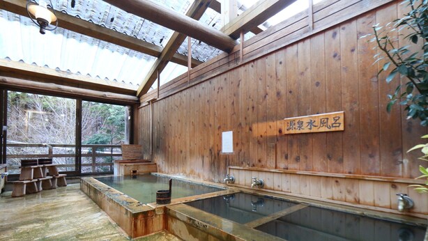 Un balneario de madera tradicional con varias tinas de agua caliente y bancos de madera.