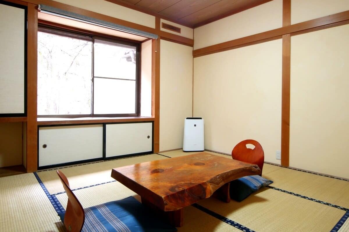 Um quarto japonês tradicional com piso de tatame, uma mesa de madeira baixa, uma cadeira vermelha e uma porta deslizante que dá para uma varanda.