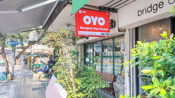 Una façana amb un rètol que diu 'OYO Bangkok Hub Hostel' i una part d'un edifici amb el rètol 'bridge'.