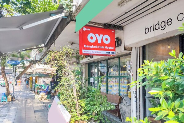 Una fachada con un letrero que dice 'OYO Bangkok Hub Hostel' y una vista parcial de un edificio con un letrero que indica 'bridge'.