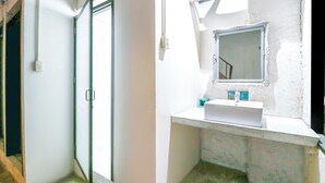 Un bany amb un lavabo blanc, un mirall i una zona de dutxa.