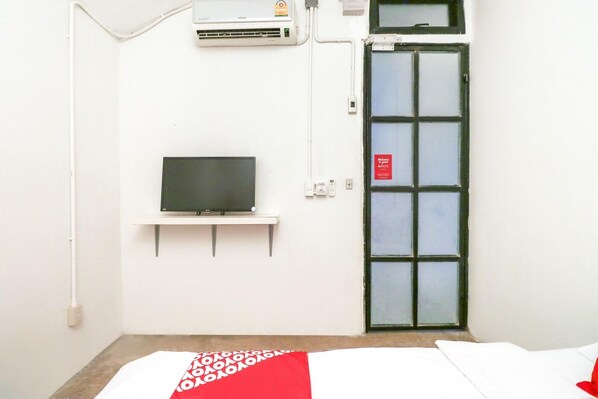 A room with a television on a white stand, a door with a frosted glass panel, and a white wall with a power outlet. - Oyo 688 Bangkok Hub Hostel (Bangkok)