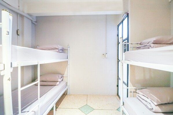 A dormitory room with bunk beds, a tiled floor, and a plain wall.