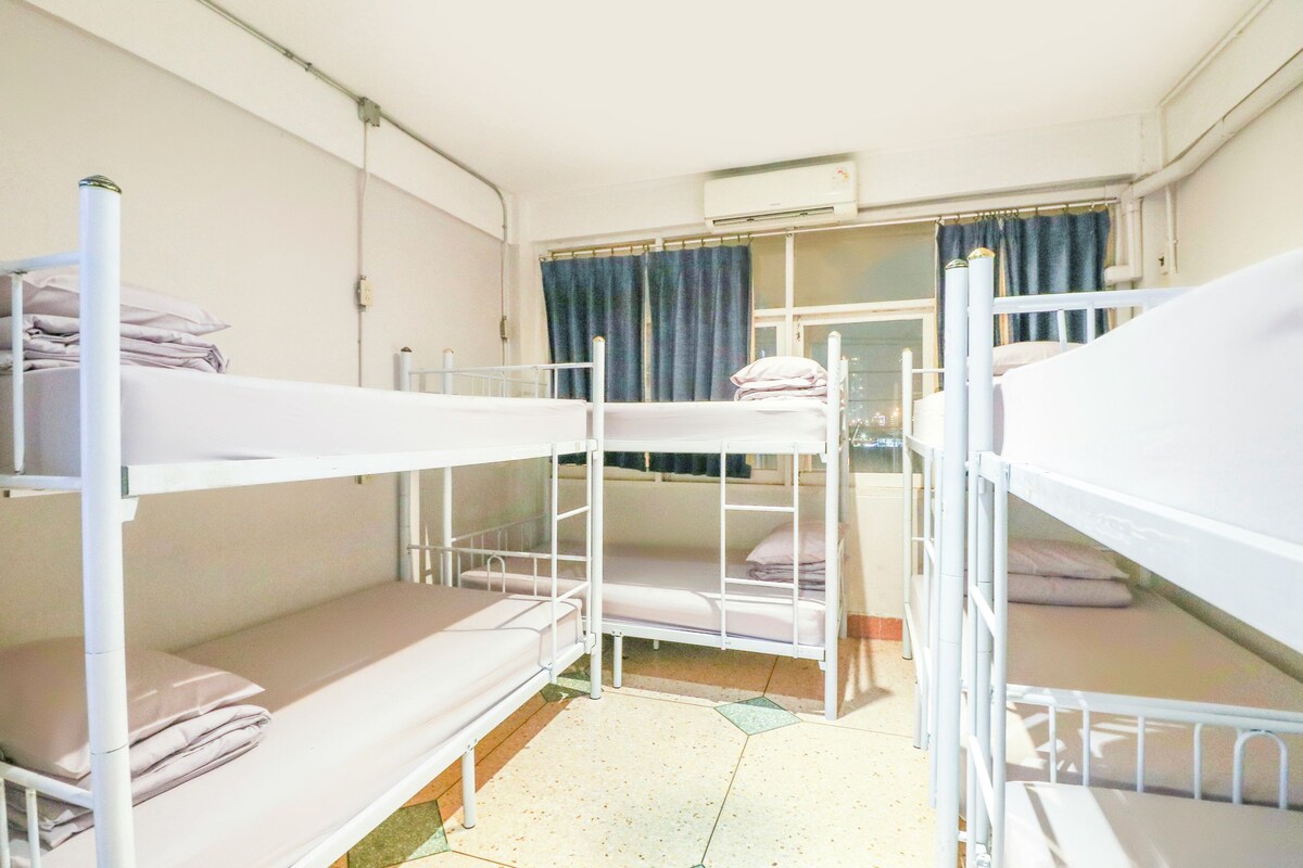 A dormitory room with bunk beds, a window with curtains, and an air conditioning unit.