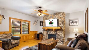 A cozy living room with a stone fireplace, wooden furniture, and a ceiling fan. - Unwind and Relax! Walk-in Log Cabin with Gas Fireplace and Screened Balcony (Branson)