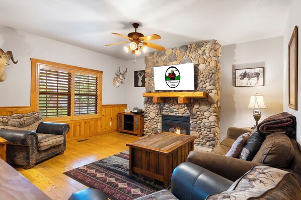 A cozy living room with a stone fireplace, wooden furniture, and a ceiling fan. - Unwind and Relax! Walk-in Log Cabin with Gas Fireplace and Screened Balcony (Branson)