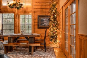 Un intérieur en bois avec une table à manger, des bancs et un sapin de Noël décoré.