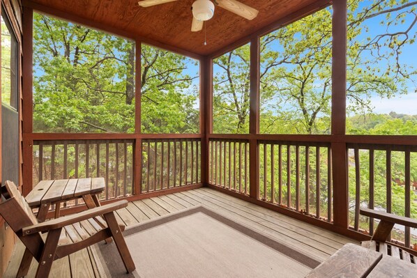 Une véranda avec une table et des chaises en bois, de grandes fenêtres et une vue sur les arbres.