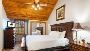 A bedroom with a wooden ceiling, a bed, a dresser, a lamp, a television, and a window with blinds. - Unwind and Relax! Walk-in Log Cabin with Gas Fireplace and Screened Balcony (Branson)