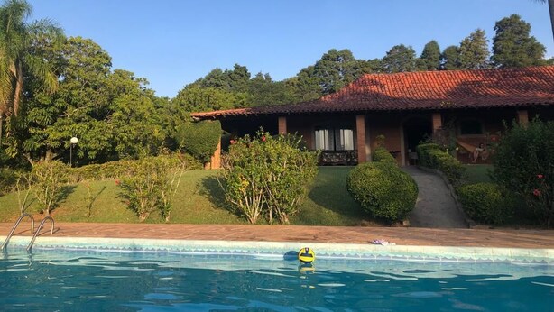 A pool with a yellow ball, surrounded by lush greenery and a house with a red roof. - WONDERFUL HOME - FAMILY LEISURE (Itu)