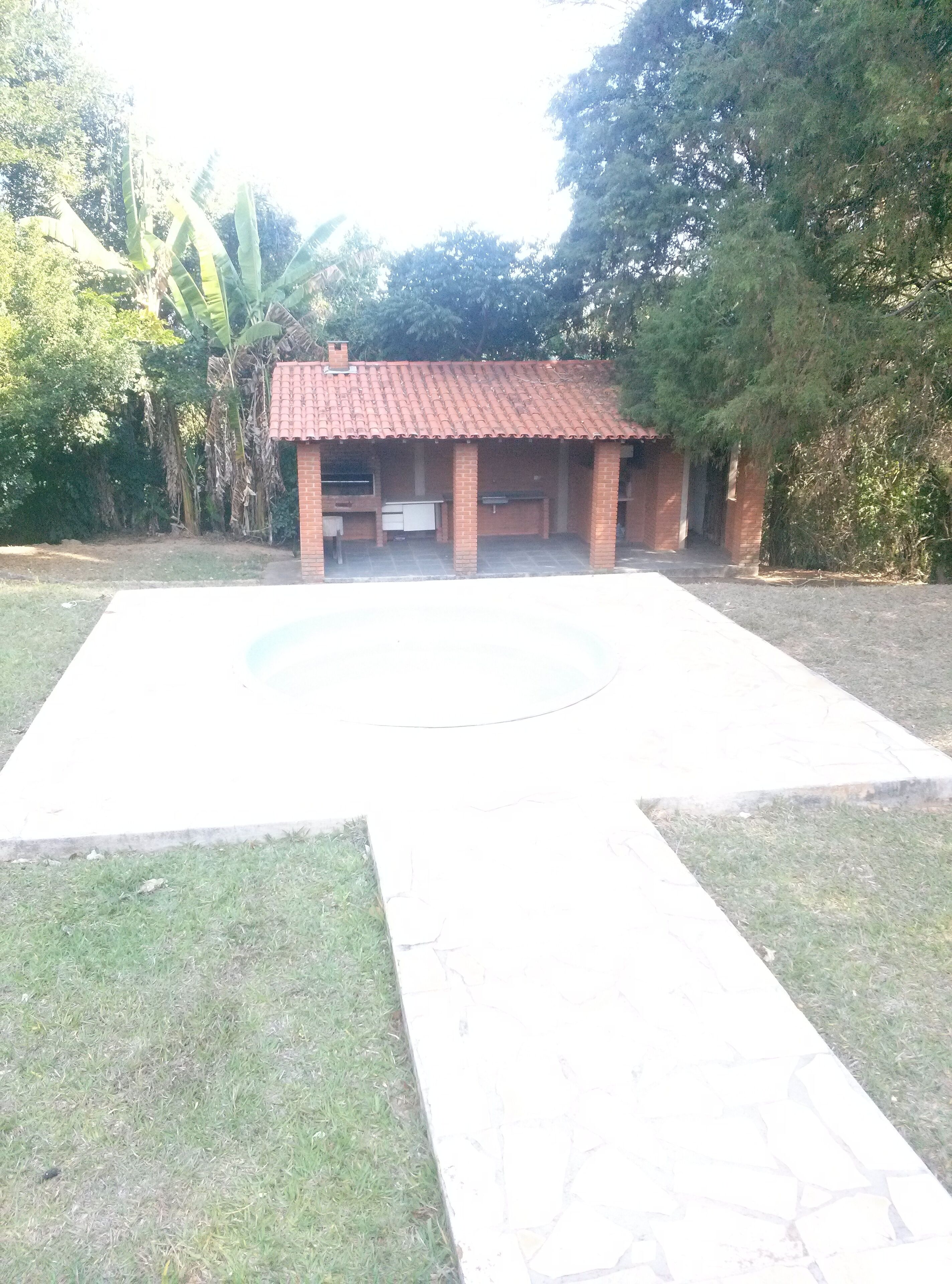 A small brick building with a tiled roof, a paved area in front, and surrounding greenery.