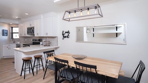 Une cuisine moderne avec des meubles blancs, une table à manger en bois et des chaises noires.