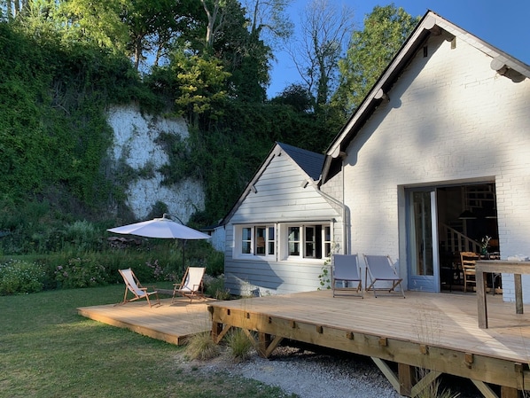 A white house with a deck, outdoor seating, and a staircase leading to the entrance. - Beautiful house in the countryside near the ocean (Longueil)