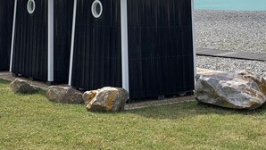 A row of black beach huts with metal roofs, positioned on a pebbled beach with a view of the sea and cloudy sky.
