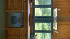 A kitchen with wooden cabinets, a stainless steel oven, and a window overlooking greenery.