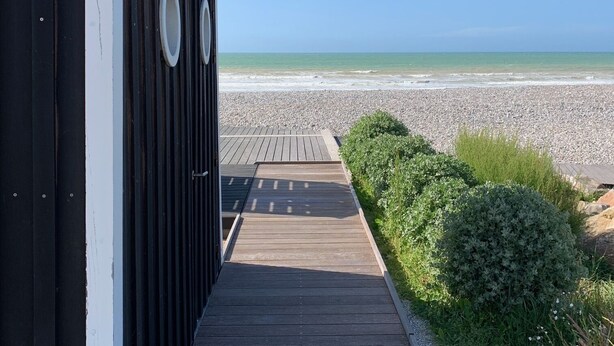 A wooden pathway leading to a building with a view of the beach.