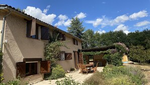 A rustic house with a patio, wooden shutters, and a garden.