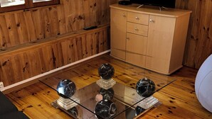 A room with wooden walls, a glass-top table with decorative spheres, a television on a wooden cabinet, and a sofa.