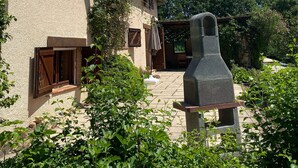 A two-story house with a stone facade, wooden shutters, and a stone bench in the garden.